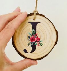 a hand holding a wooden ornament with flowers on it and the letter j