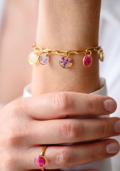 a close up of a person's hand wearing a gold bracelet with pink and purple stones