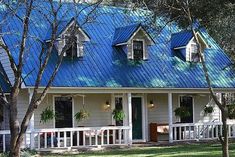 a small white house with blue roof and windows on the front porch is surrounded by trees