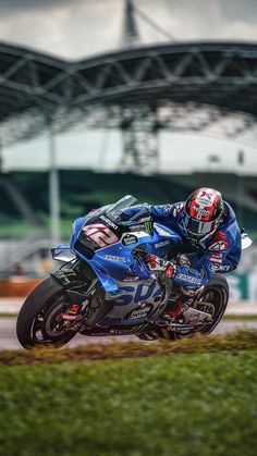 a man riding on the back of a blue motorcycle down a race track in front of a stadium