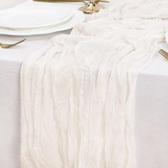 the table is set with white linens and gold place settings for two people to eat