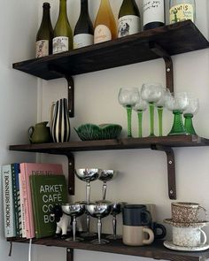 two shelves with wine glasses, cups and other items on top of them in front of a white wall