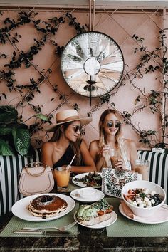 two women sitting at a table with plates of food and drinks in front of them