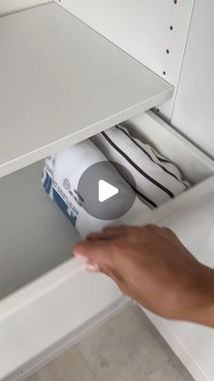 someone is opening the bottom shelf of a white cabinet with black and white items in it