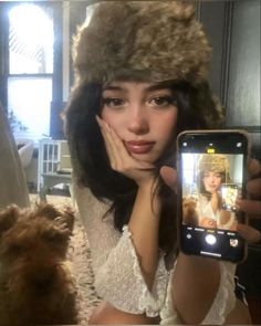 a woman is taking a selfie with her cell phone while wearing a furry hat