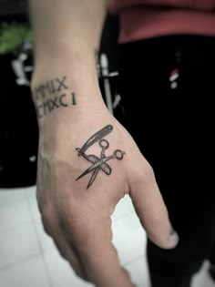 a person's hand with a tattoo on it holding a pair of scissors in their left hand