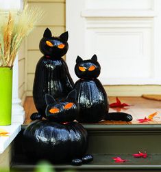 two black cat statues sitting on top of a step next to a green planter