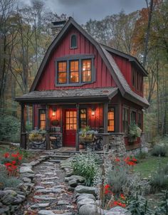 a small red house in the woods with flowers and rocks on the path leading to it