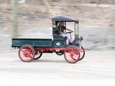 an old fashioned car driving down the road in front of some rocks and dirt on a sunny day