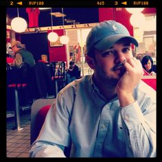 a man sitting at a table in a restaurant talking on a cell phone and holding his hand to his face