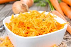 a white bowl filled with shredded carrots on top of a table next to vegetables