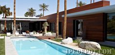 an empty swimming pool surrounded by palm trees and lawn furniture in front of a modern home