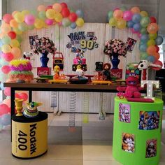 a table topped with lots of balloons and stuffed animals next to a wall covered in pictures