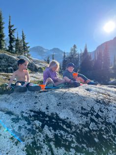 two young boys sitting on top of a rock next to each other in the mountains