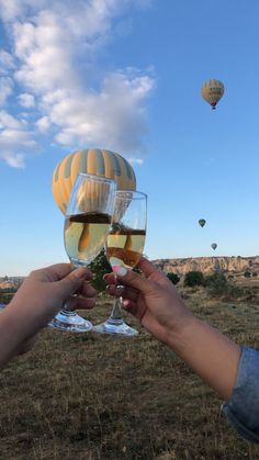 two people toasting with wine glasses in front of hot air balloons on a sunny day