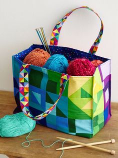 a multicolored bag sitting on top of a wooden table next to yarn and knitting needles