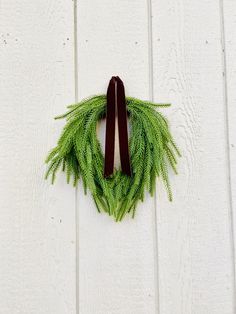 a green wreath hanging on the side of a white wooden wall with a brown ribbon