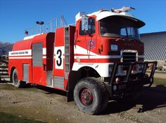 a red and white fire truck parked in front of a large building with mountains in the background