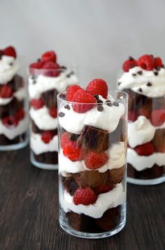 some desserts are in a glass on a table with raspberries and whipped cream