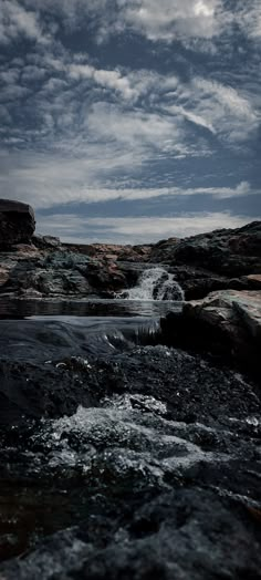 the water is running down the rocks in the river and there are clouds above it