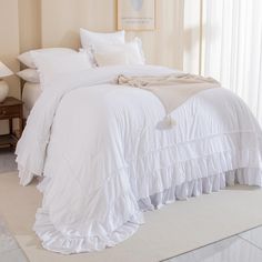 a bed with white ruffled bedspread and pillows in a light colored room