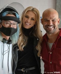 two men and a woman wearing face masks pose for a photo with a man in a motorcycle helmet