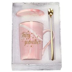 a pink marbled coffee mug with gold lettering and a spoon in the box that says,'fairy godmoter '