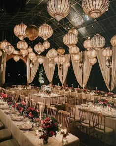 a room filled with lots of tables covered in white linens and hanging lanterns above them