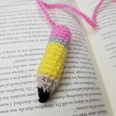 a crocheted pencil laying on top of an open book with pink and yellow yarn