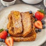 french toast with berries and powdered sugar on a plate next to two cups of coffee