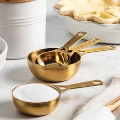 gold measuring cups and spoons are sitting on a marble countertop next to pie ingredients