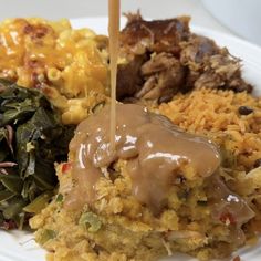 a white plate topped with meat covered in gravy next to rice and greens