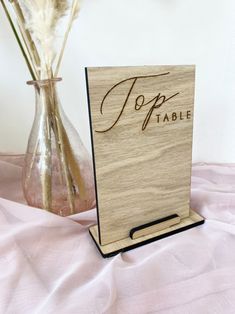 a wooden table card holder with the word jopp on it next to a vase filled with dried flowers