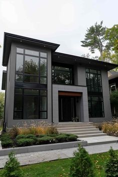 a modern house with lots of windows and plants in the front yard, along with steps leading up to it