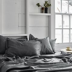 a bed with gray sheets and pillows next to a window