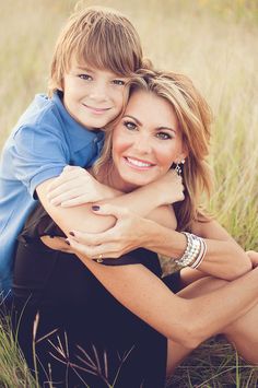 a woman and boy are sitting in the tall grass together, posing for a photo