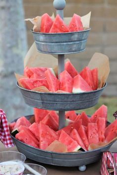 watermelon slices are arranged in three tiered trays on a picnic table