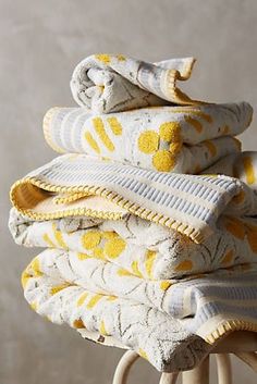 a stack of yellow and white towels sitting on top of a wooden stool next to a wall