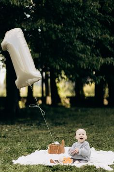 a baby sitting on a blanket in the grass with a white balloon attached to it