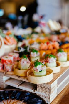 a table topped with lots of different types of sushi and other foods on wooden trays