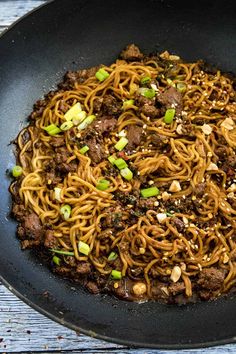 a wok filled with noodles and meat on top of a wooden table