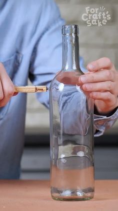 a person holding a wooden stick in front of a glass bottle with water inside it