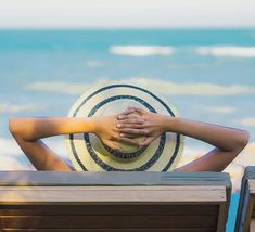 a woman sitting on top of a beach chair next to the ocean holding her hands behind her head