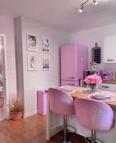 a kitchen with pink appliances and pictures on the wall behind the bar stools in front of the counter