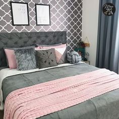 a bed with pink and grey pillows in a bedroom next to two pictures on the wall