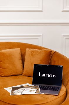 a laptop computer sitting on top of a brown couch in front of a white wall