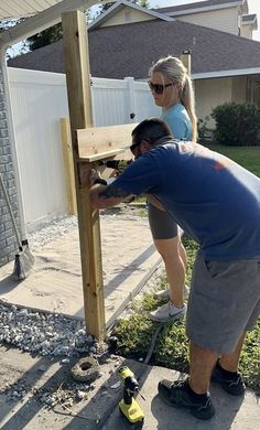 two people working on a wooden post in front of a house with a cordless drill