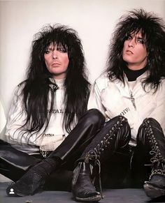 two people sitting on the ground with long hair and leather pants, one wearing black boots