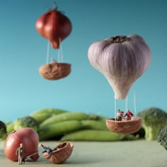 three hot air balloons floating in the sky with vegetables below them and people on top