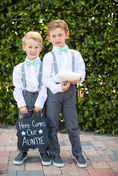 two young boys wearing suspenders and bow ties are holding a sign that says here comes our aontre